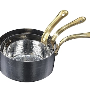 May include: A set of three hammered stainless steel saucepans with brass handles. The saucepans are nested together, with the smallest saucepan on top.