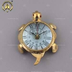 May include: A gold-colored turtle-shaped clock with a white face and Roman numeral markings. The clock face has a small red and gold emblem with the text "SMITHS LONDON".