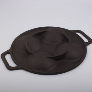 Puede incluir: Una sart&eacute;n de hierro fundido negra con cuatro moldes redondos para hacer pasteles individuales u otros productos horneados. La sart&eacute;n tiene dos asas.