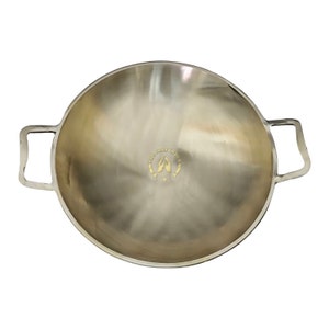 May include: A large, round, silver-colored cooking pan with two handles. The pan has a smooth, shiny surface and the words "HINDU HOLY INDIA" are engraved on the bottom.