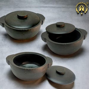 May include: Three black stone bowls with lids. The bowls are round and have two handles on each side. The lids have a small knob on top. The bowls are made of a dark, rough stone.