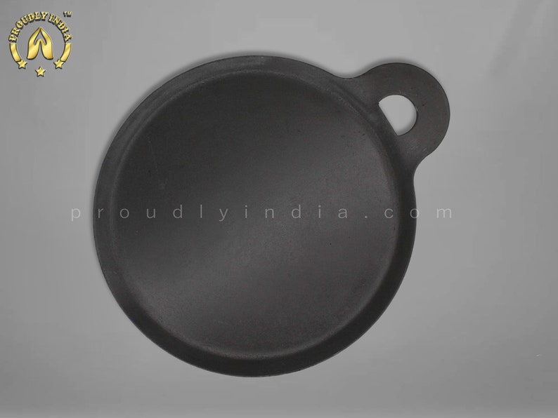 K&ouml;nnte beinhalten: Eine schwarze Gusseisen-Dosa-Pfanne mit einem einzigen Griff. Die Pfanne ist rund und hat einen leicht erh&ouml;hten Rand. Der Griff ist an der Seite der Pfanne befestigt und hat ein kleines Loch.