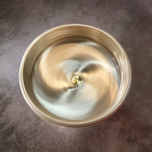 May include: A silver bowl with a swirling pattern on the inside. The bowl has a gold logo in the centre that says "Holy India" with a star on either side of the logo.