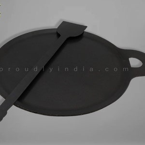 K&ouml;nnte beinhalten: Eine schwarze Gusseisen-Dosa-Pfanne mit einem Griff und einem passenden schwarzen Spatel. Die Pfanne ist rund und hat einen leicht erh&ouml;hten Rand. Der Spatel ist lang und d&uuml;nn mit einem abgerundeten Ende.