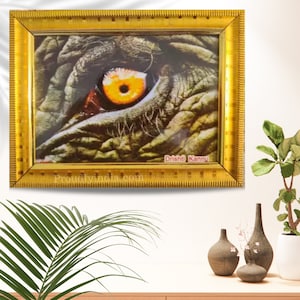 Puede incluir: Una impresi&oacute;n enmarcada de un primer plano de un ojo de elefante. El ojo es amarillo y marr&oacute;n con una pupila negra. La impresi&oacute;n est&aacute; enmarcada en un marco dorado con el texto "Dristhi Kannu" y "Proudlyindia.com" en la parte inferior.
