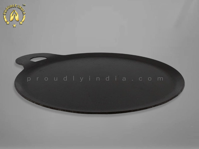 K&ouml;nnte beinhalten: Eine schwarze Gusseisen-Dosa-Pfanne mit einem Griff. Die Pfanne ist rund und hat einen leicht erh&ouml;hten Rand. Der Text "proudlyindia.com" ist auf die Pfanne gedruckt.