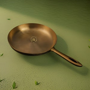 May include: A gold-colored frying pan with a long handle. The pan has a logo that says "Proudly India" with a hand symbol and three stars.