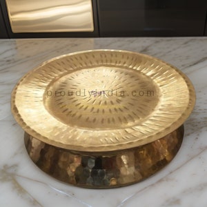 May include: A round, hammered brass serving tray with a raised, fluted rim. The tray has a decorative, hammered finish and is ideal for serving snacks or appetizers.