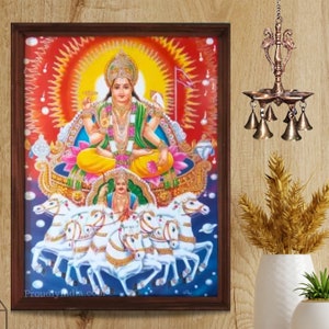 Könnte beinhalten: Eine gerahmte Illustration der hinduistischen Gottheit Surya, dem Sonnengott, der einen von sieben weißen Pferden gezogenen Wagen fährt. Er ist mit einem goldenen Heiligenschein und einer gelben Robe dargestellt, die auf einer Lotusblume sitzt. Der Hintergrund ist leuchtend rot und orange mit einem Sonnenstrahlenmuster. Das Bild ist in einem dunkelbraunen Holzrahmen gerahmt.