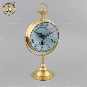 May include: A gold-toned tabletop clock with a round face and Roman numeral markings. The clock face has a blue background with a white ship illustration and the text "SUPERIOR SHIP TIMEKEEPER".