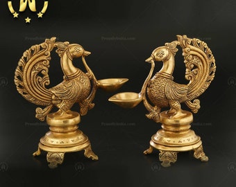 Op de afbeelding: Een paar gouden metalen pauwen-vormige olielampen met ingewikkelde details. Elke lamp heeft een ronde basis met drie poten en een pauwenontwerp met een opgeheven staart.