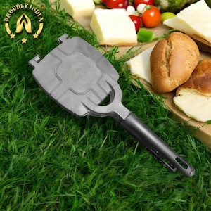 Puede incluir: Una prensa de sándwich de mano de metal gris con un mango negro. La prensa está sobre un lecho de hierba verde.