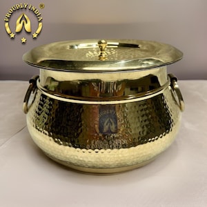 May include: A gold hammered brass serving dish with a lid. The dish has two handles on the sides and a decorative knob on the lid.