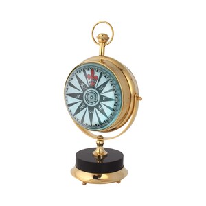 May include: A gold compass with a blue face and a black and white compass rose. The compass has a fleur-de-lis design and is on a black and gold stand.