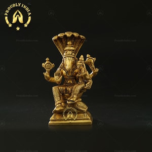 May include: A gold-colored metal statue of a Hindu deity, sitting on a throne with a cobra hood. The deity has a human-like body with an animal head and is holding a staff in one hand.