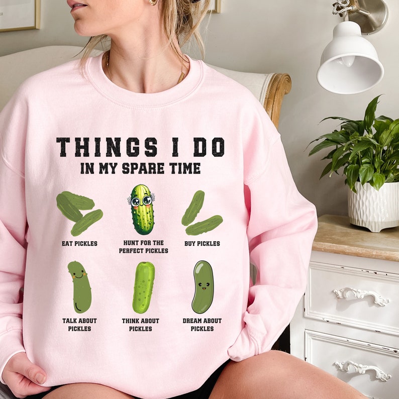 May include: Pink sweatshirt with the text "THINGS I DO IN MY SPARE TIME" and a series of cartoon pickles with different expressions and activities, such as "EAT PICKLES", "HUNT FOR THE PERFECT PICKLES", "BUY PICKLES", "TALK ABOUT PICKLES", "THINK ABOUT PICKLES", and "DREAM ABOUT PICKLES".