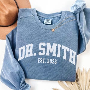 May include: A blue sweatshirt with the text "DR. SMITH EST. 2023" in white.