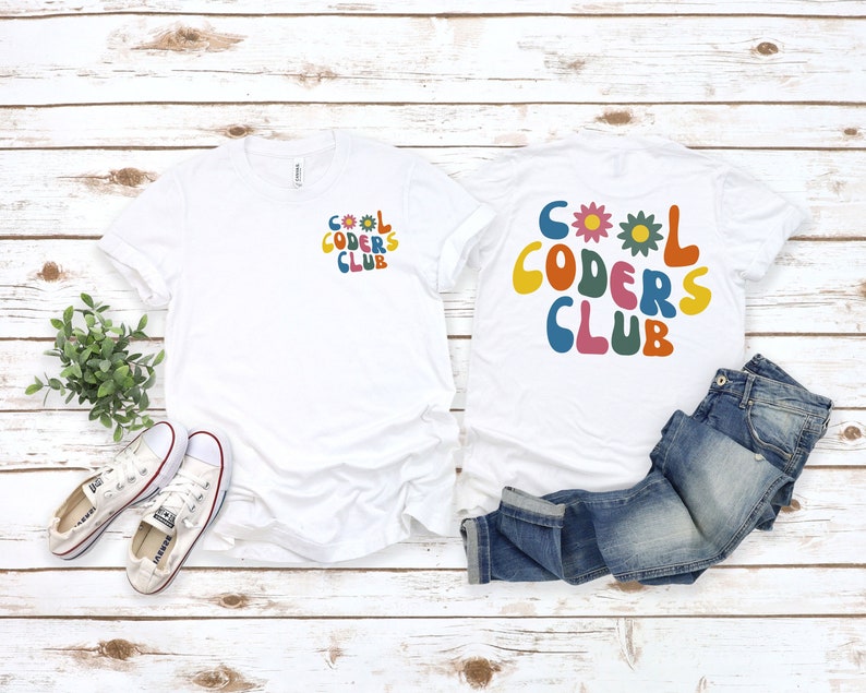 May include: Two white t-shirts with the text "Cool Coders Club" in colourful, retro-style letters. One shirt has the text on the front and the other has the text on the back. The shirts are laid out on a white wooden surface with a pair of white trainers and blue jeans.