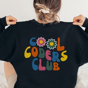 Peut inclure: Sweat-shirt noir avec un graphisme r&eacute;tro color&eacute; qui dit "Cool Coders Club" avec des fleurs.