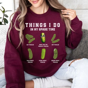 May include: Burgundy sweatshirt with the text "THINGS I DO IN MY SPARE TIME" and a series of cartoon pickles with text describing activities related to pickles, such as "EAT PICKLES", "HUNT FOR THE PERFECT PICKLES", "BUY PICKLES", "TALK ABOUT PICKLES", "THINK ABOUT PICKLES", and "DREAM ABOUT PICKLES".