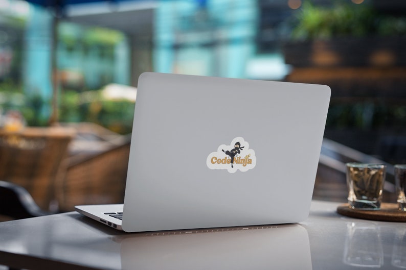 May include: A silver laptop computer with a sticker of a cartoon ninja kicking a star with the text "Code Ninja" in gold letters.