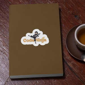 May include: A brown notebook with a sticker of a cartoon ninja in black clothing with a white cloud and the text "Code Ninja" in orange.