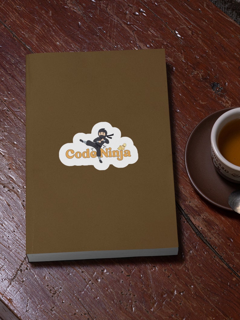 May include: A brown notebook with a sticker of a cartoon ninja in black clothing with a white cloud and the text "Code Ninja" in orange.