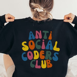 Peut inclure: Sweat-shirt noir avec un graphisme coloré qui dit "Anti Social Coders Club" dans une police rétro.