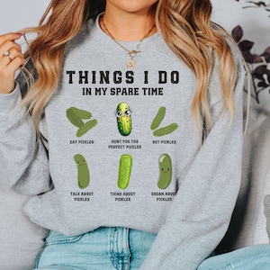 May include: Gray sweatshirt with the text "THINGS I DO IN MY SPARE TIME" and a series of cartoon pickles with different expressions and activities, including "EAT PICKLES", "HUNT FOR THE PERFECT PICKLES", "BUY PICKLES", "TALK ABOUT PICKLES", "THINK ABOUT PICKLES", and "DREAM ABOUT PICKLES".