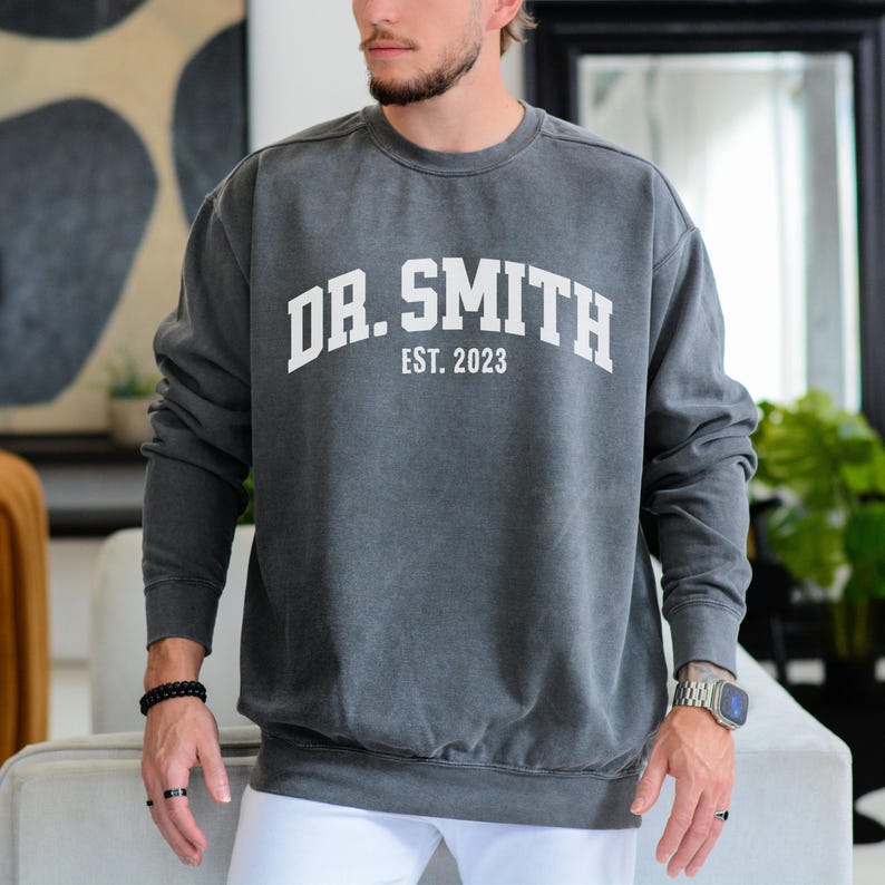 May include: A dark gray sweatshirt with a white print that reads "DR. SMITH EST. 2023" in an arched font.