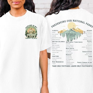 May include: White t-shirt with a green nature scene and the text "Nature is my happy place" on the front. The back of the shirt has a list of Canadian national parks and the text "Preserving our National Parks. Take only pictures, leave only footprints."