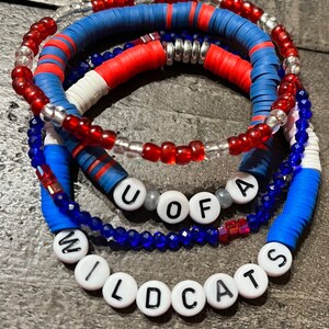 May include: A set of four bracelets with red, white, and blue beads. The bracelets spell out "U of A Wildcats".
