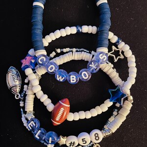 May include: A set of four bracelets featuring white and blue beads, with charms including footballs, stars, and the word "COWBOYS". The bracelets also include the name "ELI" and the numbers "#58".