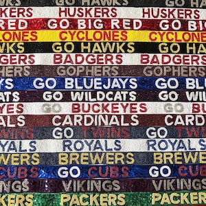 May include: A colorful beaded banner with the names of various sports teams and the phrase "Go" in front of each team name. The banner is made of beads in various colors, including red, white, blue, gold, and black.