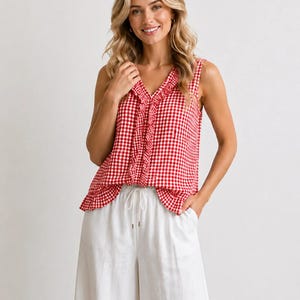 Può includere: Un top senza maniche a quadri rossi e bianchi con scollo a V e dettaglio a balze. Il top è abbinato a pantaloni bianchi a gamba larga con vita con coulisse. L'outfit è casual ed estivo.