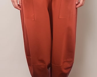 Pode incluir: Uma calça de perna larga cor ferrugem com grandes bolsos nas laterais. A calça tem cintura com cordão e caimento solto. A modelo está usando tênis branco.