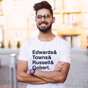 Può includere: Una maglietta bianca con il testo "Edwards & Towns & Russell & Gobert." stampato in blu.