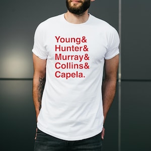 May include: White t-shirt with red text that reads "Young & Hunter & Murray & Collins & Capela."