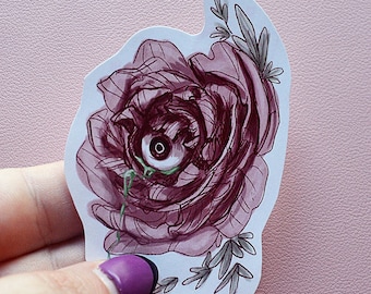 Könnte beinhalten: Ein Aufkleber mit einer dunkelroten Rose mit einem Augapfel in der Mitte. Der Augapfel hat eine weiße Iris und eine schwarze Pupille. Grüne Ranken und Blätter sind ebenfalls im Design enthalten. Der Aufkleber hat einen weißen Rand auf rosa Hintergrund.