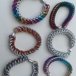Peut inclure: Six bracelets en cotte de mailles disposés en deux colonnes. Les bracelets présentent des anneaux métalliques entrelacés dans diverses combinaisons de couleurs, dont arc-en-ciel, rouge, or, argent, bleu et violet, avec un fermoir magnétique.