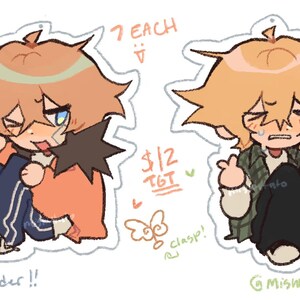 May include: Two 2.5 inch cartoon character keychains. One keychain features a character with orange hair and an orange jacket, the other keychain features a character with blonde hair and a green jacket. The text "7 EACH" and "$12 TGT" is written on the image.