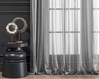 May include: A black side table with a round top and a decorative base. Two white and gray marble rings are on stands on the table. The table is in front of a window with sheer gray curtains.