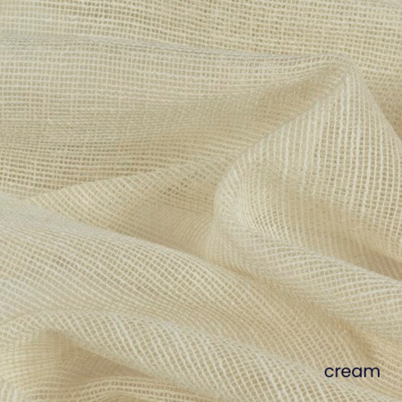 May include: Cream colored fabric with a woven texture. The fabric is folded and draped, showing the texture and color.