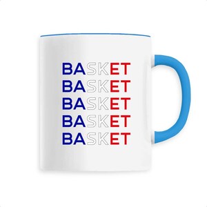 May include: White ceramic mug with a blue rim and handle. The mug features the word "BASKET" repeated five times in a stacked pattern, with each word in a different colour: blue, white, red, white, and blue.