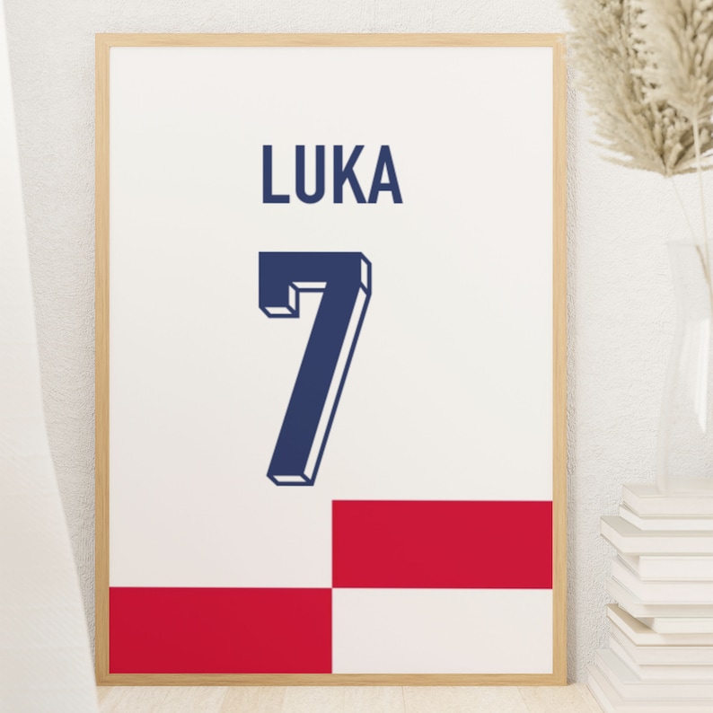 May include: A framed print with a white background, a navy blue number "7" and the name "LUKA" in navy blue. The bottom of the print has a red and white checkered pattern.