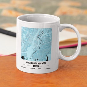 Peut inclure: Une tasse en céramique blanche avec une carte de la ville de New York et le parcours du marathon de New York. La tasse porte l'inscription "Marathon de New York" et "42,195KM".