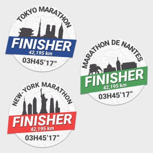 Op de afbeelding: Drie ronde marathon finisher stickers. Elk heeft een silhouet van een stadsgezicht, het woord "FINISHER", de afstand van 42.195 km en een tijd. De stickers zijn voor de marathons van Tokio, New York en Nantes.