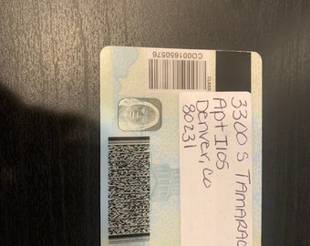 Könnte beinhalten: Ein blauer und weißer Führerschein des Colorado Department of Revenue mit dem Text "3300 S TAMARAC DR. Apt Ilos Denver, Co 80231" und einem Barcode.