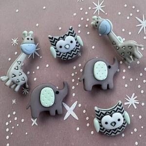 May include: A collection of whimsical animal-shaped embellishments. The assortment includes two giraffes, two elephants, and two owls. The giraffes are gray with blue accents, the elephants are gray with mint green accents, and the owls are black and white with mint green accents.