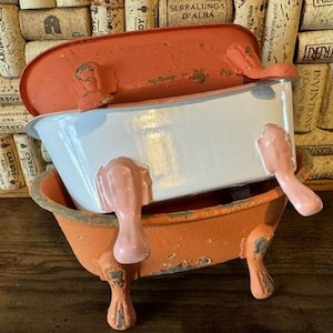 May include: Three decorative, vintage-style bathtubs stacked on top of each other. The top tub is coral, the middle one is white, and the bottom one is orange. Each tub has pink claw feet. The background features corks.